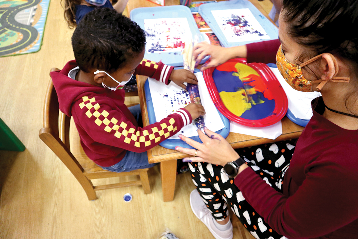 pre-school teacher helping child fingerpaint
