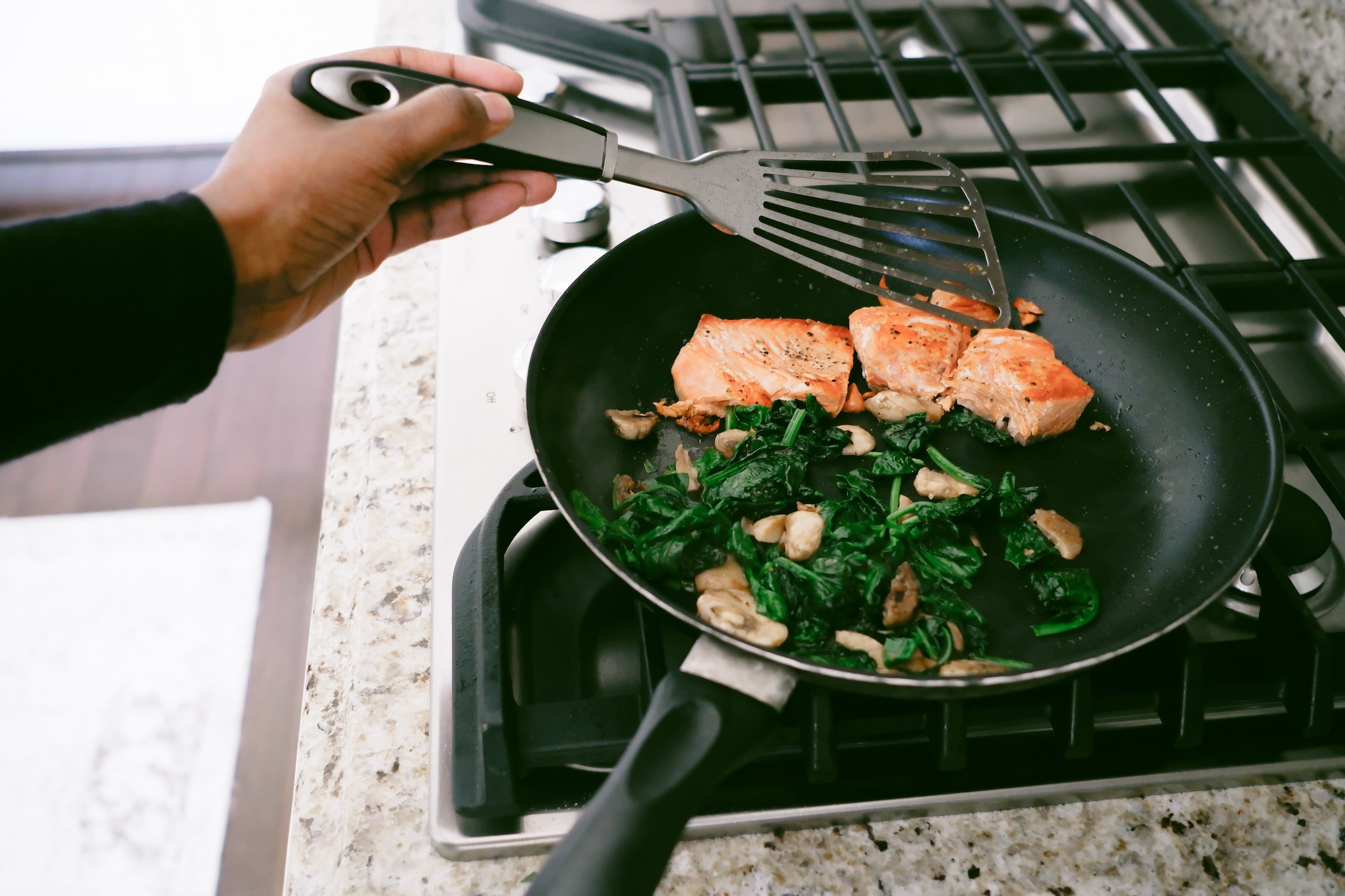 Salmon and greens being cooked in a pan on a stovetop