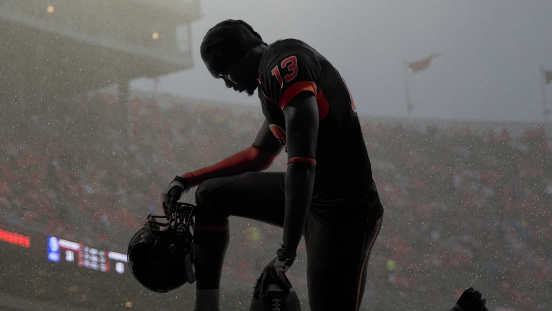 College football player kneeling on the field with helmet removed