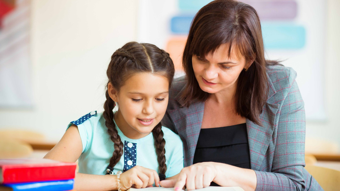 teacher tutoring a child in reading at a school desk